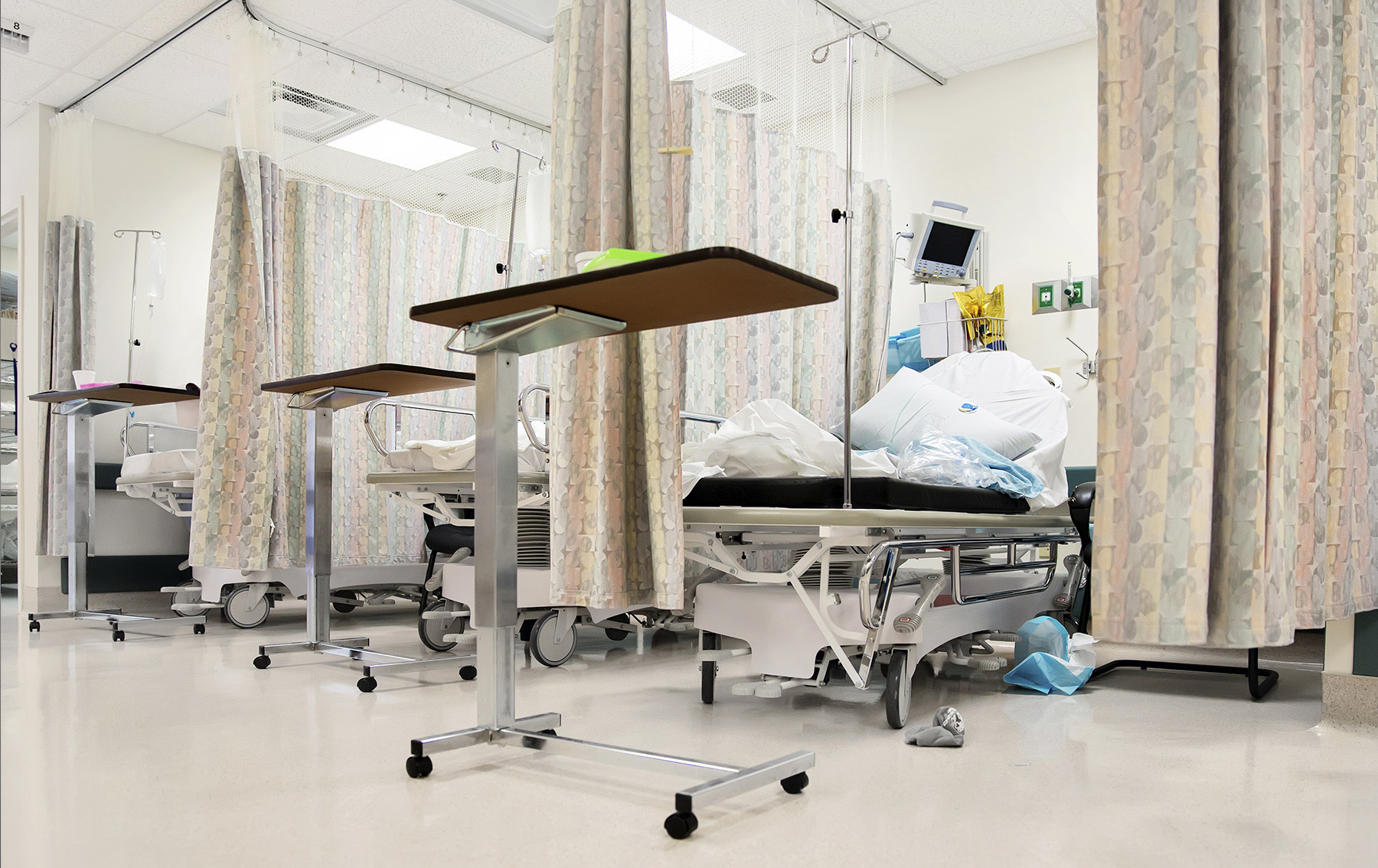 Hospital emergency room bays separated by privacy curtains with waste piled on the bed